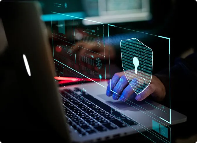 Hands typing on a laptop overlaid with a holographic shield icon for system protection.