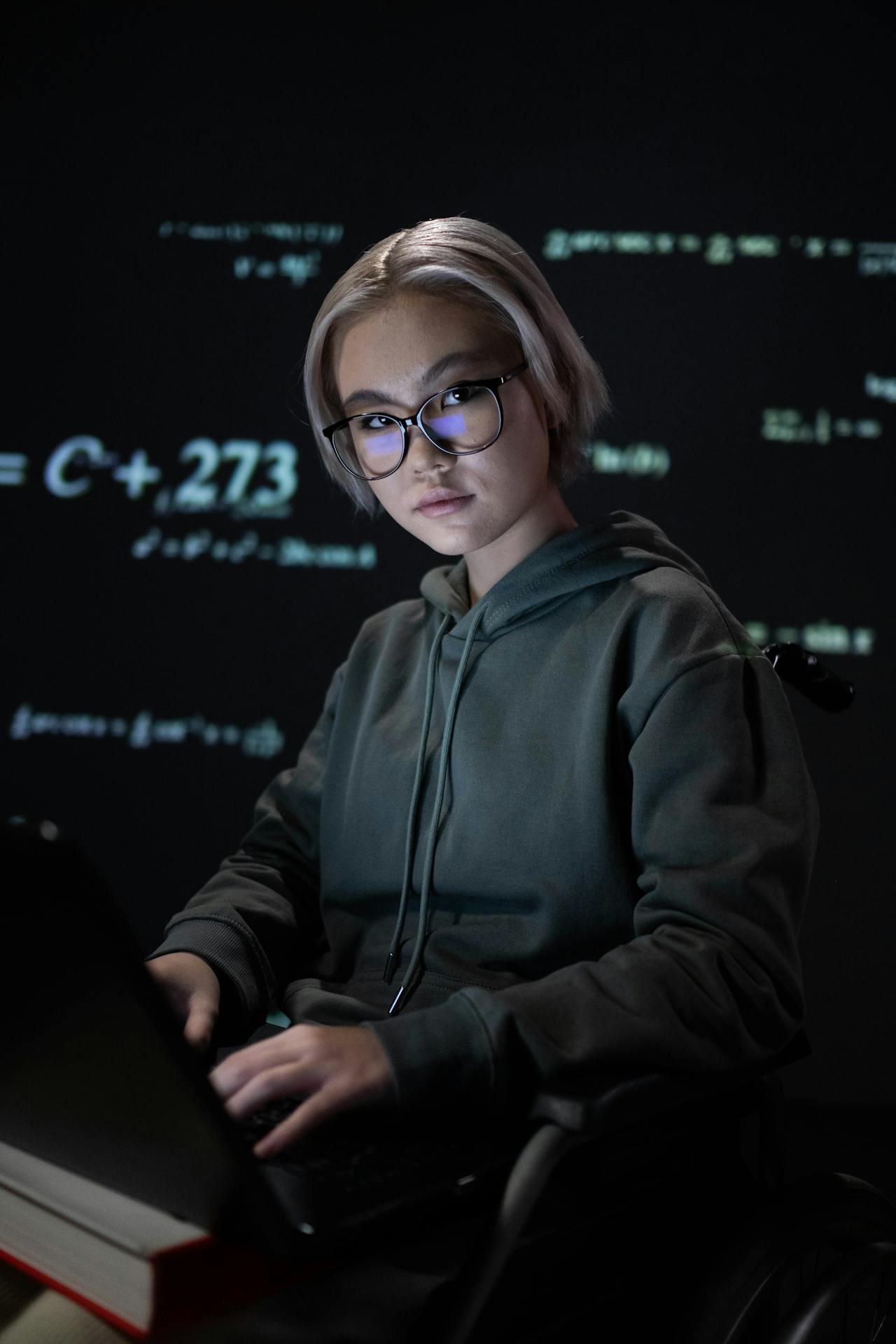 Hoodie-clad coder in glasses working on a laptop amid projected lines of code.