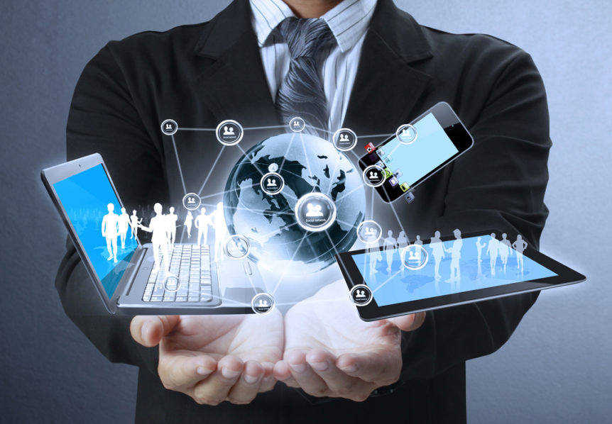 Businessperson cupping a holographic globe flanked by interconnected mobile and laptop devices.